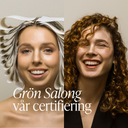 Två leende kvinnor på Green Heads, en med hårpapper i håret och en med naturliga lockar, som illustrerar salongens Grön Salong-certifierade, giftfria hårvård.