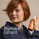 Kvinna med kort kopprigt hår håller Green Heads Sea Salt Mist i handen, omslagsbild till blogg om risprotein i hårvård och volymgivande produkter.